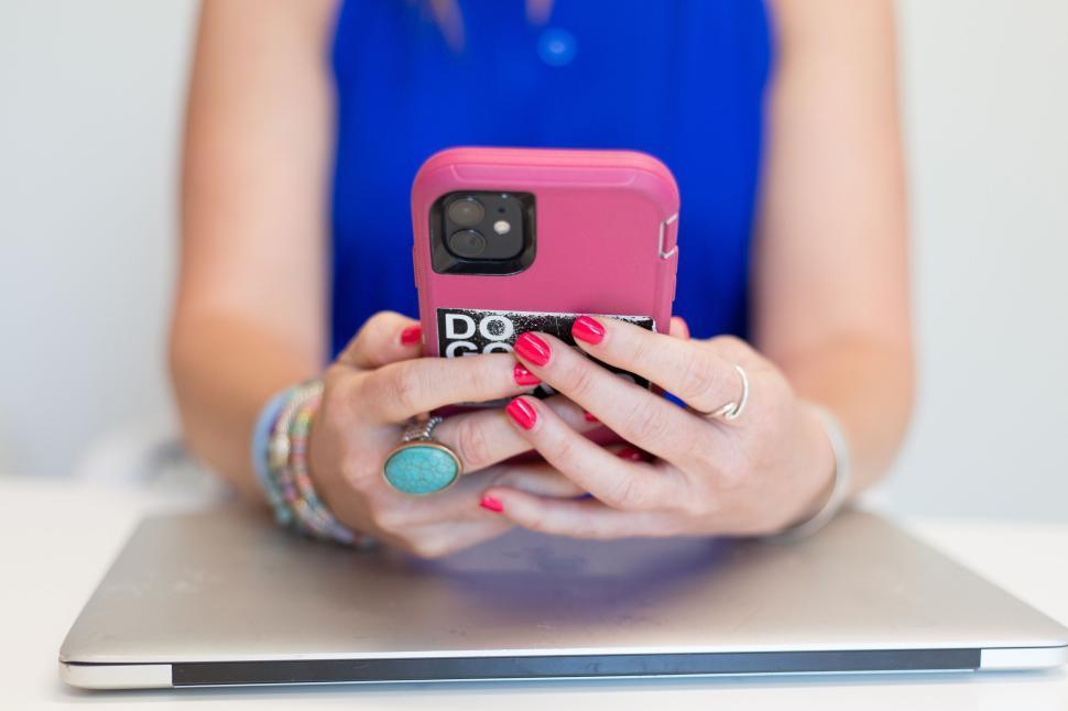 Free Image of Woman with pink phone and turquoise ring working on laptop at desk 