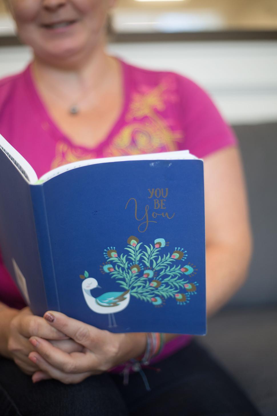 Free Image of Person reading a book titled  You Be You  while smiling subtly. 