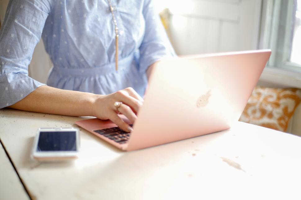 Free Image of Person typing on a pink laptop with smartphone beside on wooden desk. 