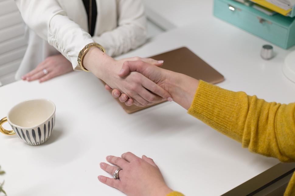 Free Image of Handshake between two individuals at a white desk in office setting 
