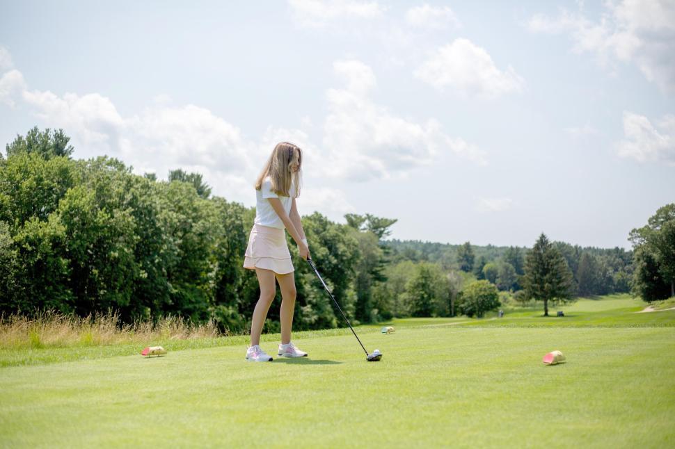 Free Image of Young girl playing golf on a sunny day on a well-maintained course. 