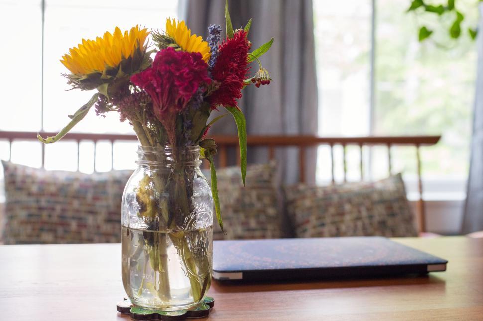 Free Image of Mason jar with fresh flowers on a table in a cozy, well-lit space. 