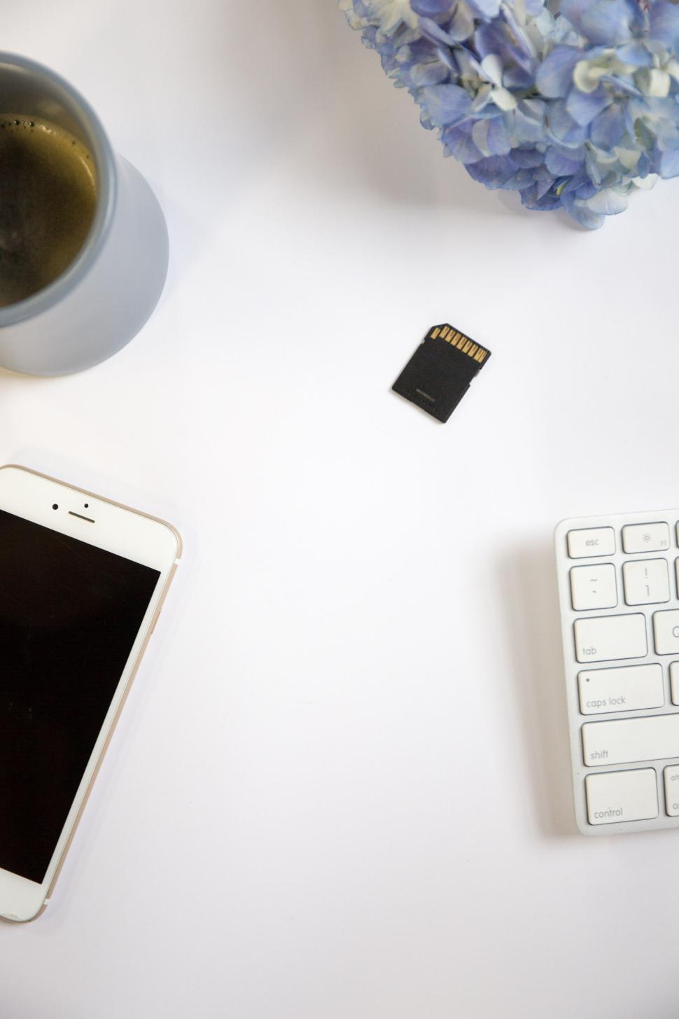 Free Image of Office desk with phone, SD card, coffee, keyboard, and flowers 