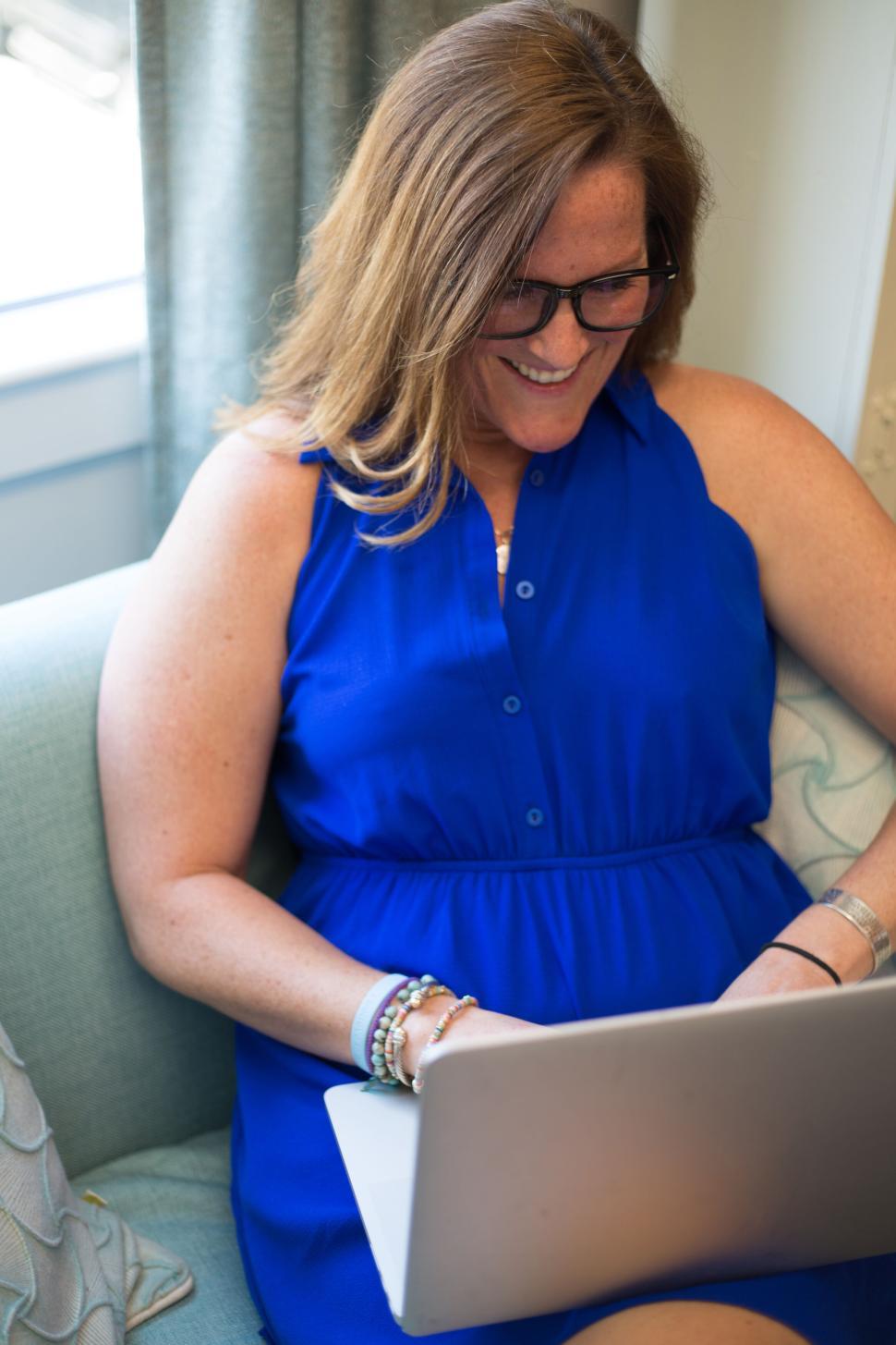 Free Image of Woman in blue dress working on laptop seated on a comfortable sofa 