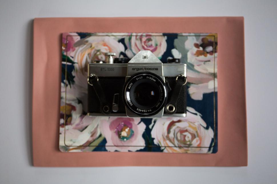 Free Image of Vintage camera on floral print paper next to a pink envelope. 