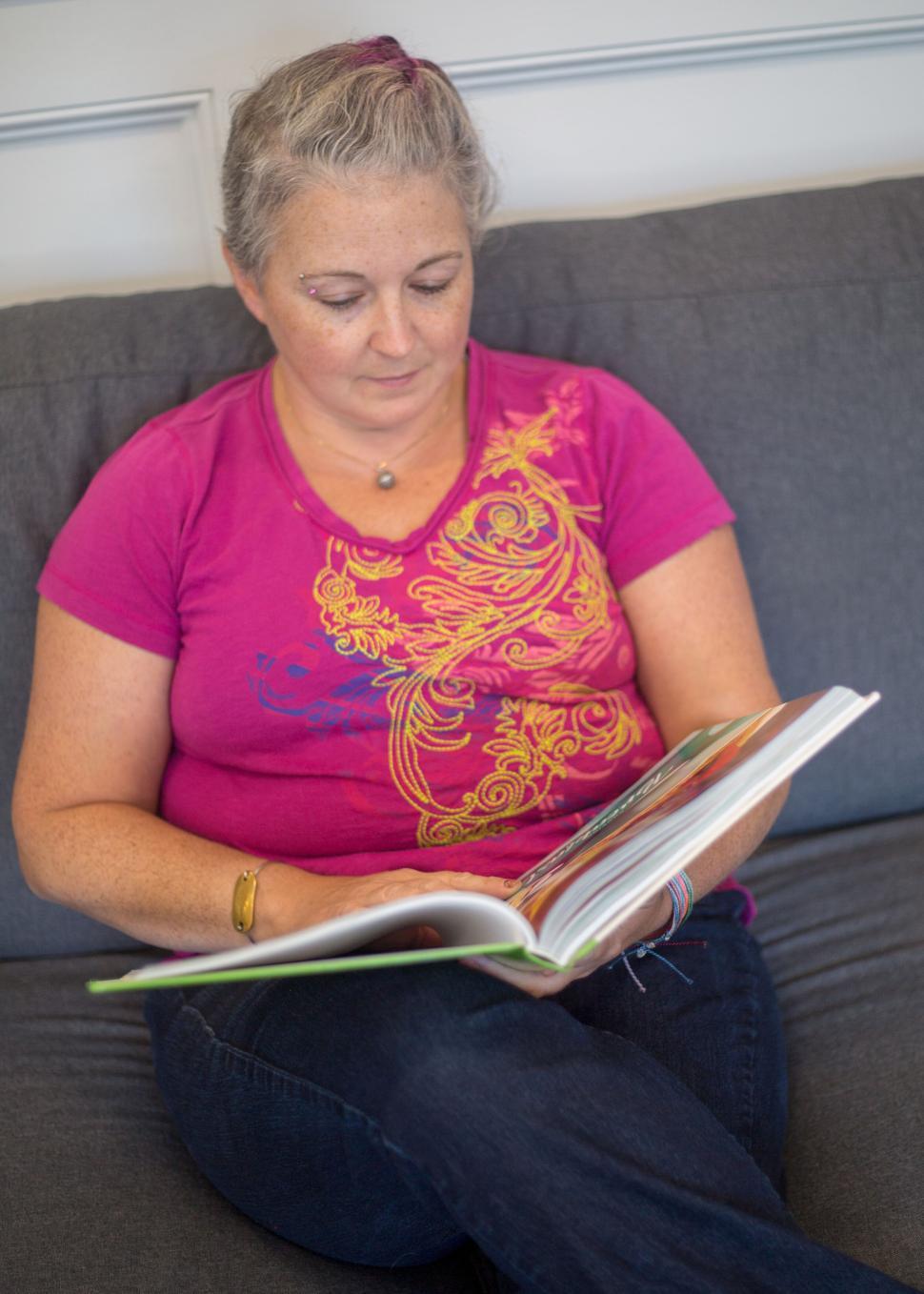 Free Image of Woman reading book on a couch, dressed in pink and jeans 