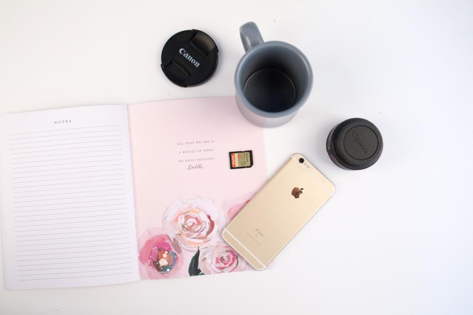 Free Image of Flat lay of notebook, camera caps, phone, SD card, and coffee mug. 