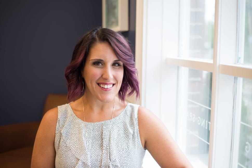 Free Image of Smiling woman with purple hair and white top by the window 