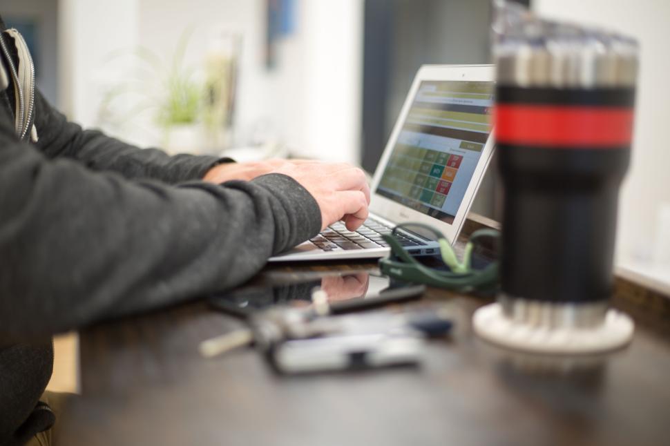 Free Image of Person typing on laptop with desk accessories and coffee tumbler 