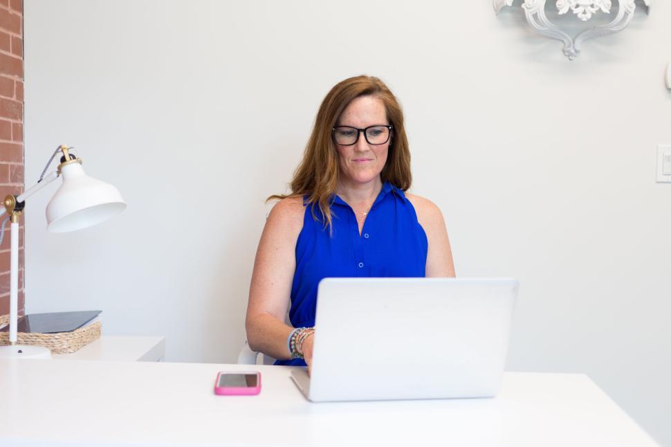 Free Image of Woman in blue blouse typing on laptop at a minimalist desk 