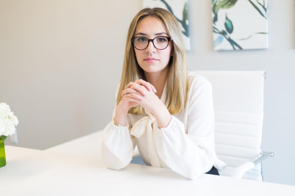 Free Image of Confident woman in glasses and white blouse at a white desk 