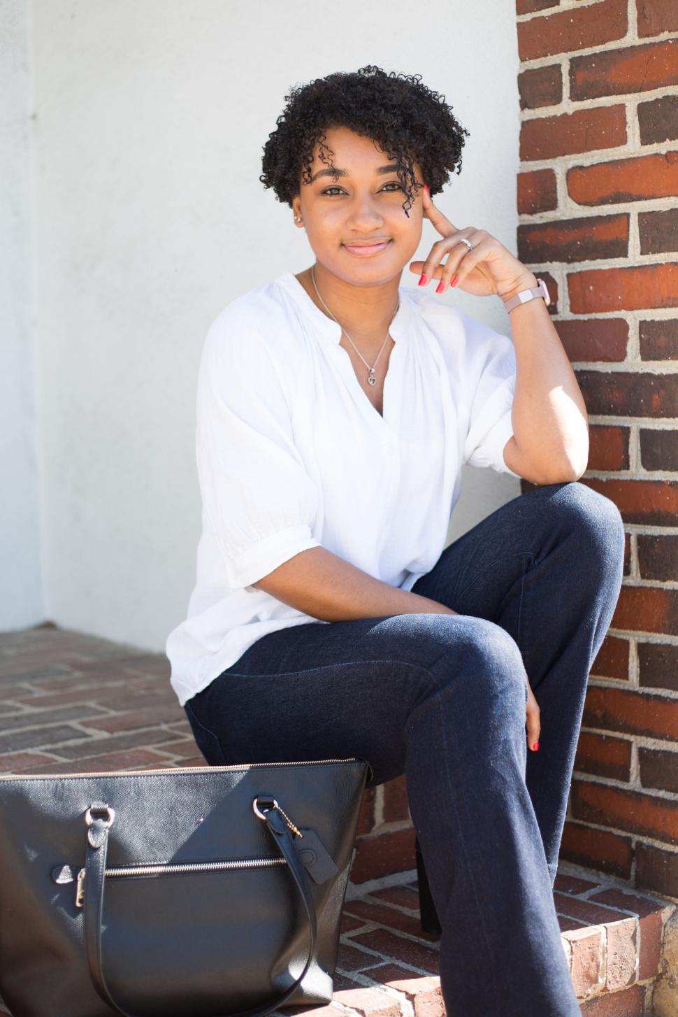 Free Image of Woman sitting on steps, wearing white blouse and dark jeans 