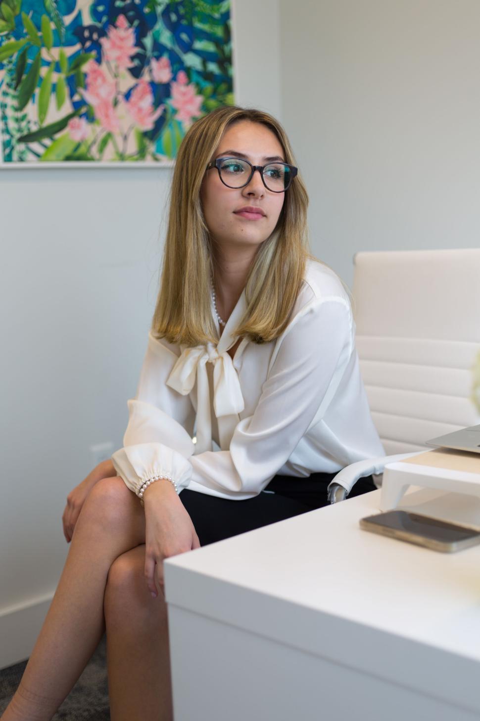 Free Image of Young woman sitting in an office setting with white blouse 