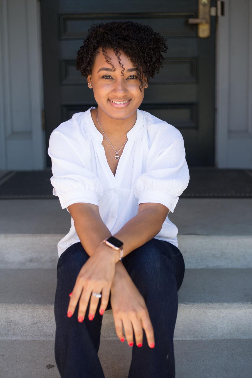 Free Image of Woman sitting on steps smiling in casual white blouse 
