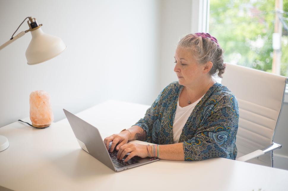 Free Image of Person typing on laptop at white desk with salt lamp and lamp. 