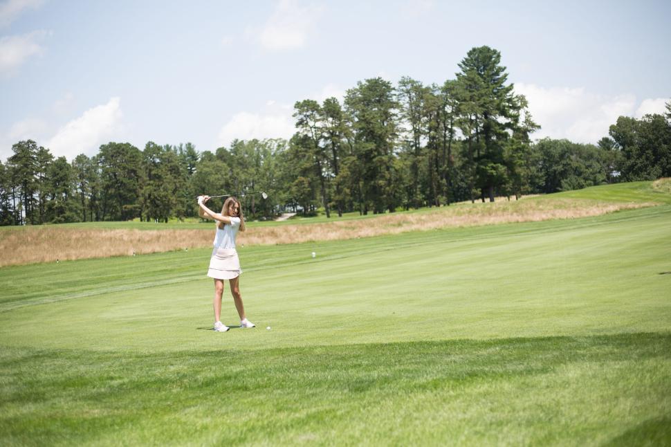 Free Image of Person wearing white dress practicing golf swing on green field. 