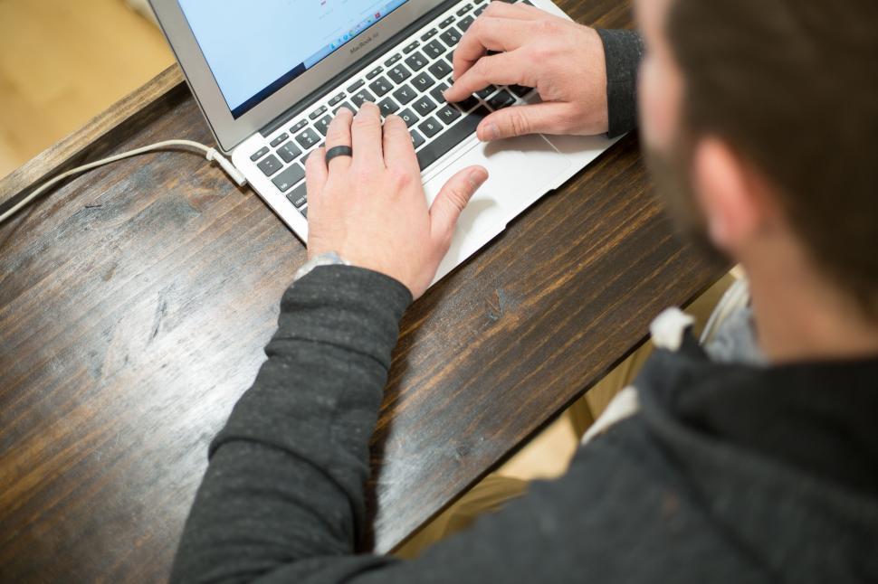 Free Image of Person typing on laptop on wooden desk wearing a black ring 