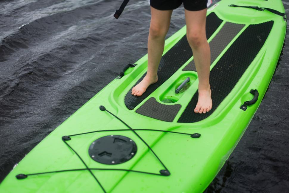 Free Image of Person standing on bright green stand-up paddleboard on water 