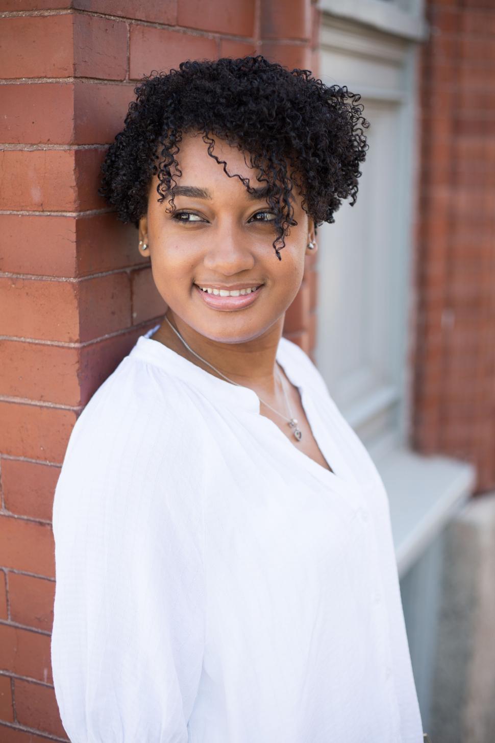Free Image of Woman standing against brick wall smiling in casual white blouse 