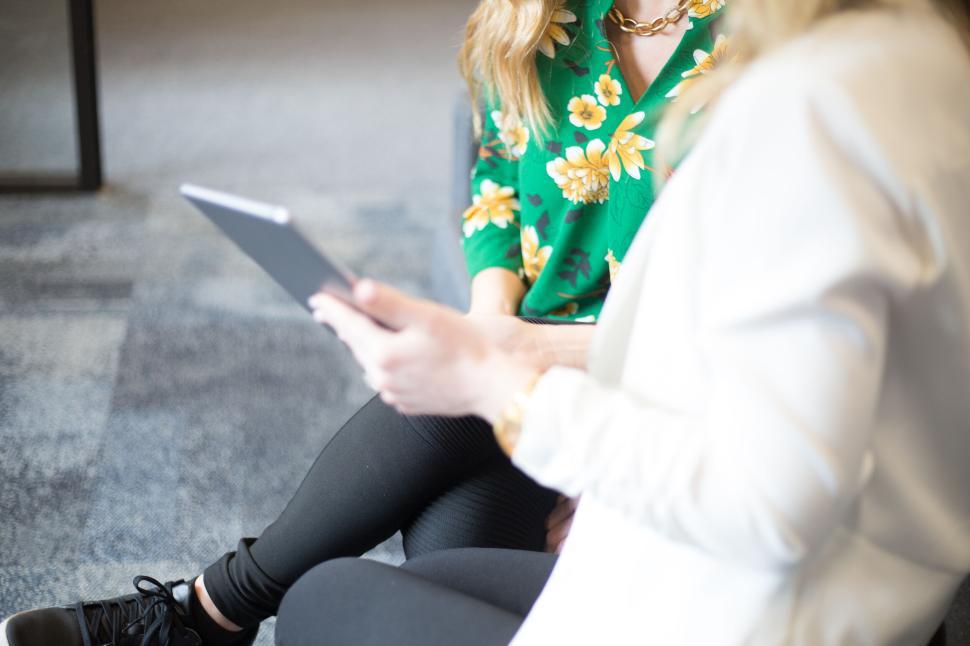 Free Image of Two women sitting and looking at a tablet wearing floral tops 