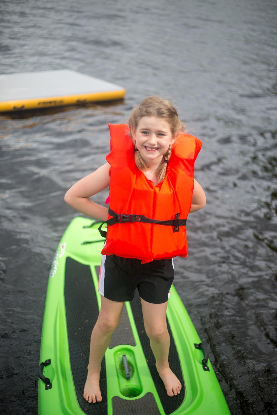 Free Image of Young girl on green paddleboard wearing red life vest smiling 