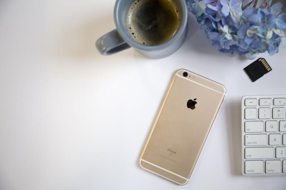 Free Image of Golden iPhone, coffee, keyboard, and flowers on a white table 