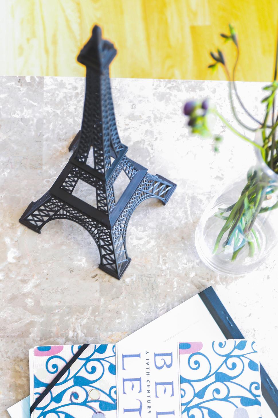 Free Image of Eiffel Tower model, book, and vase on a white and marble surface 