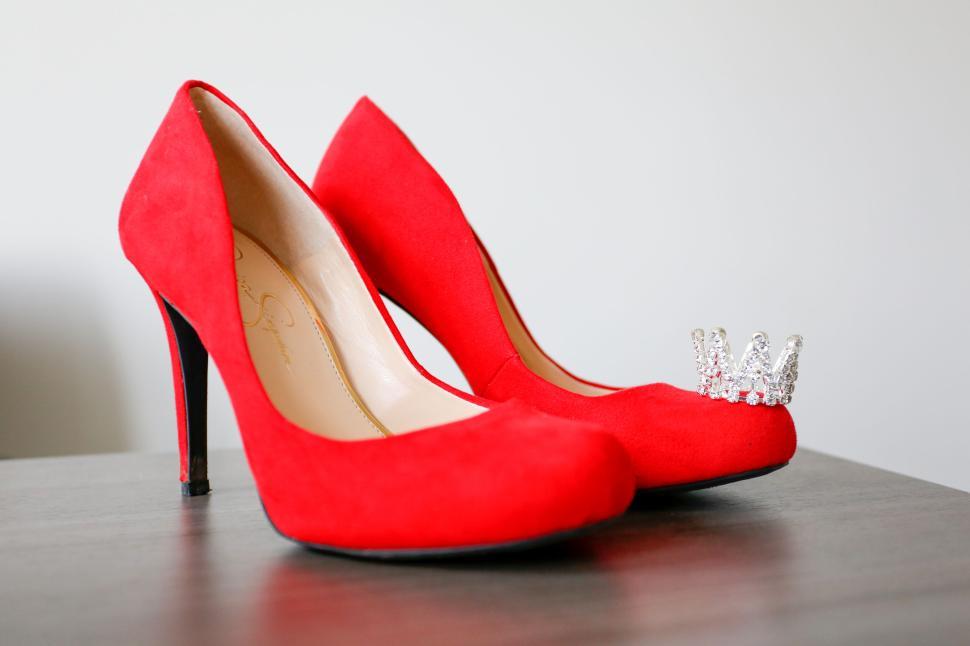 Free Image of Pair of red high heels with a small crown on one shoe, indoors. 