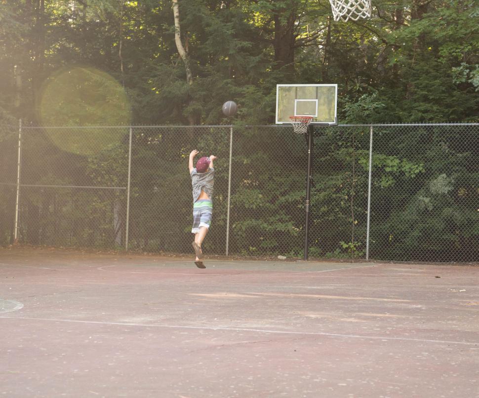 Free Image of Young boy jumping to shoot basketball on outdoor court in summer 