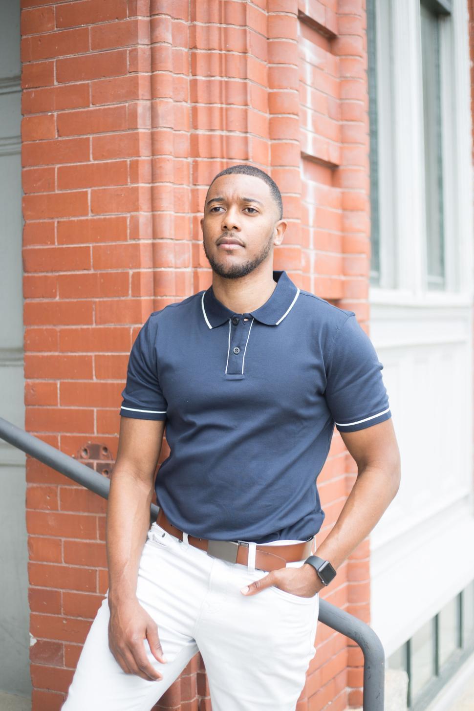 Free Image of Man standing against red brick wall in blue polo shirt outdoors 
