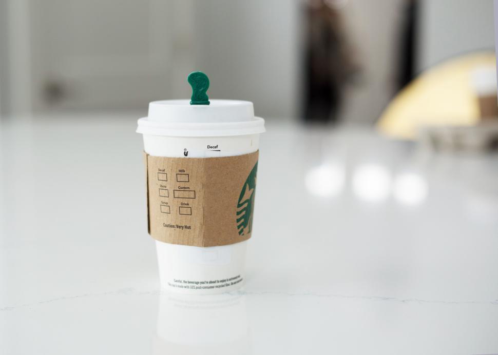 Free Image of Starbucks coffee cup with sleeve on white table, focus on cup lid 