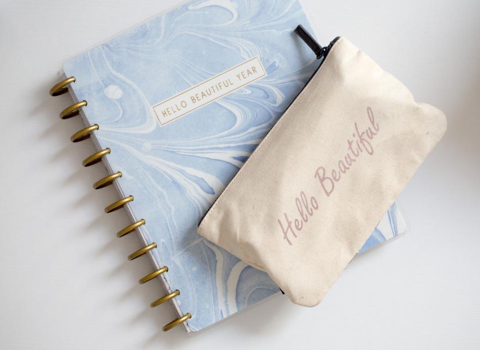 Free Image of Journal and pouch with text  hello beautiful year  on white desk 