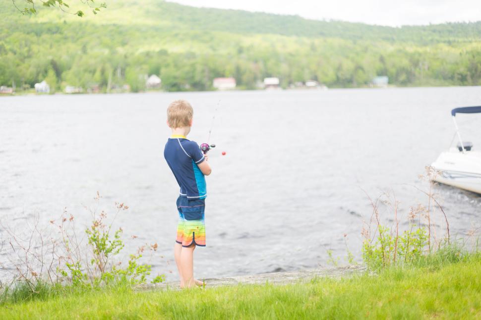 Free Image of Young boy fishing by a serene lake on a sunny summer day. 