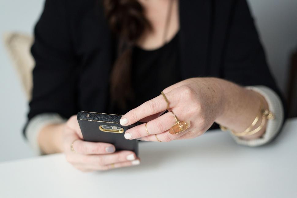 Free Image of Woman using smartphone with rings on fingers in a business setting. 