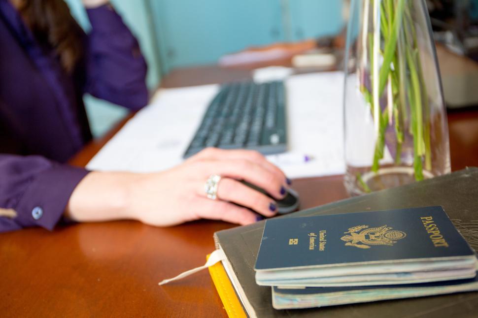 Free Image of Hand using a computer mouse next to a US passport on a desk 