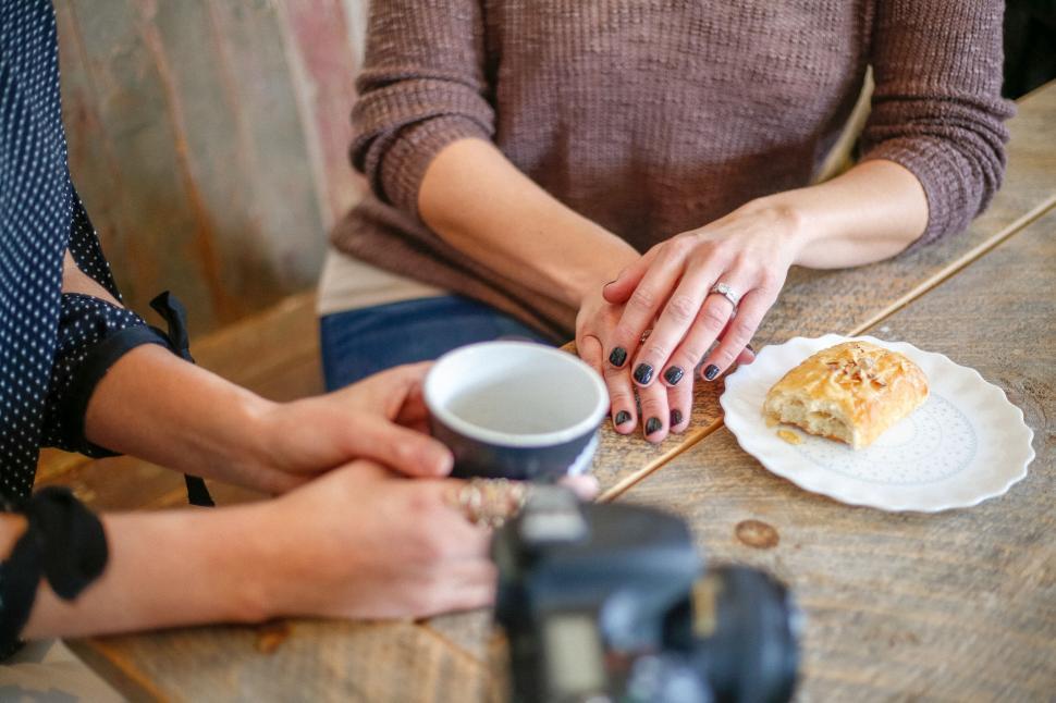 Free Image of Two women sharing a moment over coffee at a rustic wooden table 