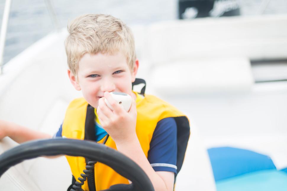 Free Image of Young boy in yellow life jacket holding radio on a boat. 