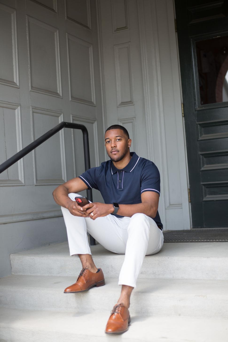 Free Image of Man in casual wear, seated with smartphone, on building steps. 