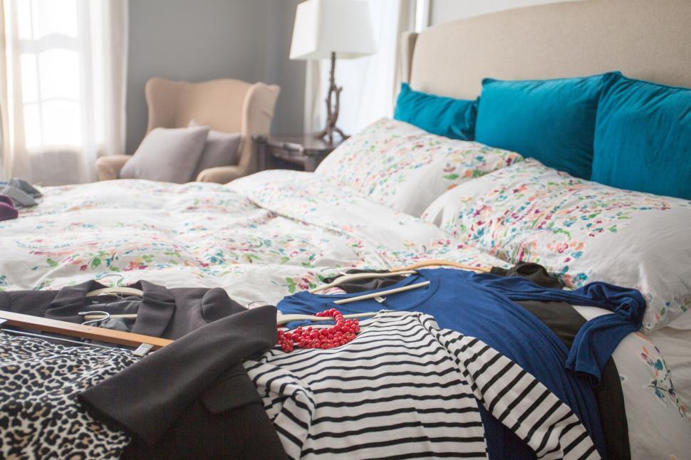 Free Image of Cozy bedroom with clothes and accessories spread on the bed 