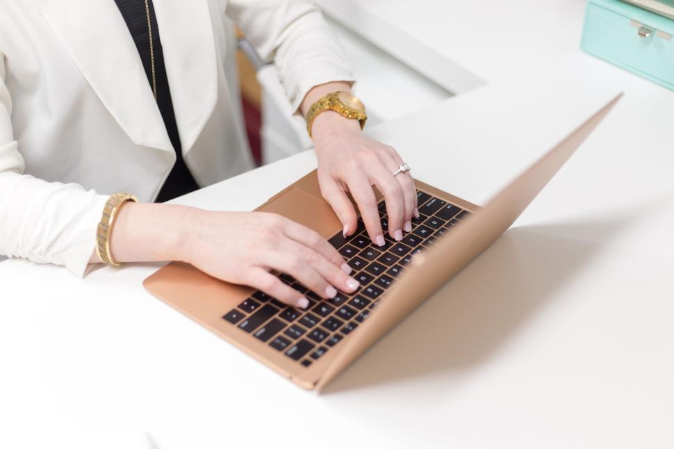 Free Image of Woman typing on a gold laptop in a white office environment 