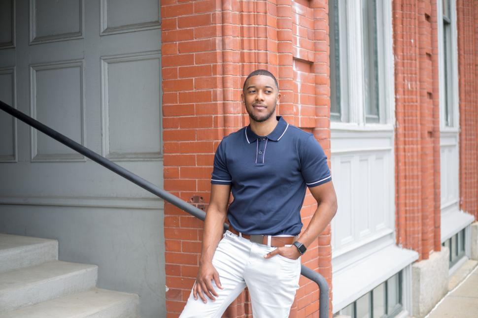 Free Image of Man in navy polo stands confidently against brick building. 