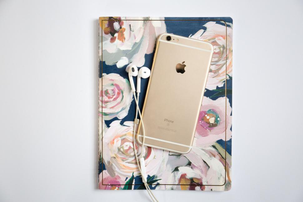 Free Image of Gold iPhone and earphones placed on a floral patterned notebook 
