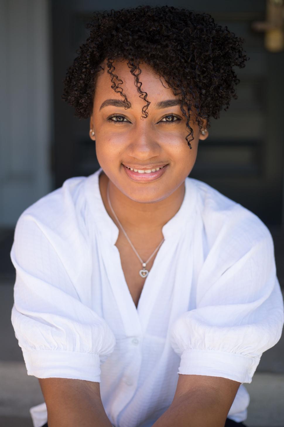 Free Image of Smiling woman in white shirt with curly hair sitting indoors 