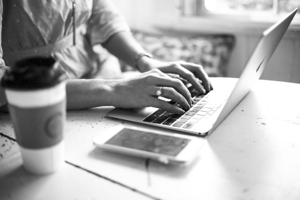 Free Image of Person typing on laptop with coffee cup in a cozy work setting. 