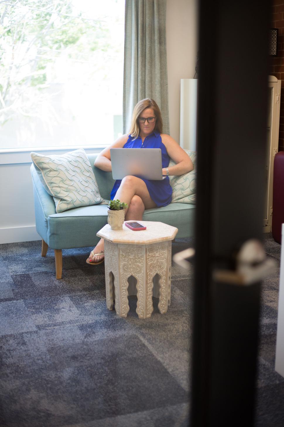 Free Image of Woman in blue dress using laptop on a couch indoors 