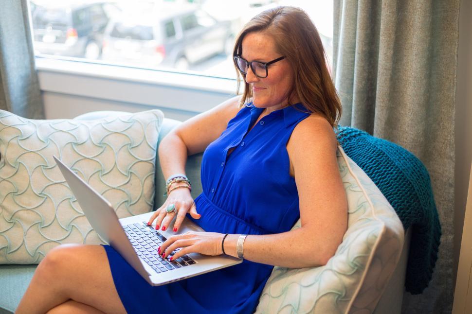 Free Image of Close-up of woman in blue dress using laptop on couch 