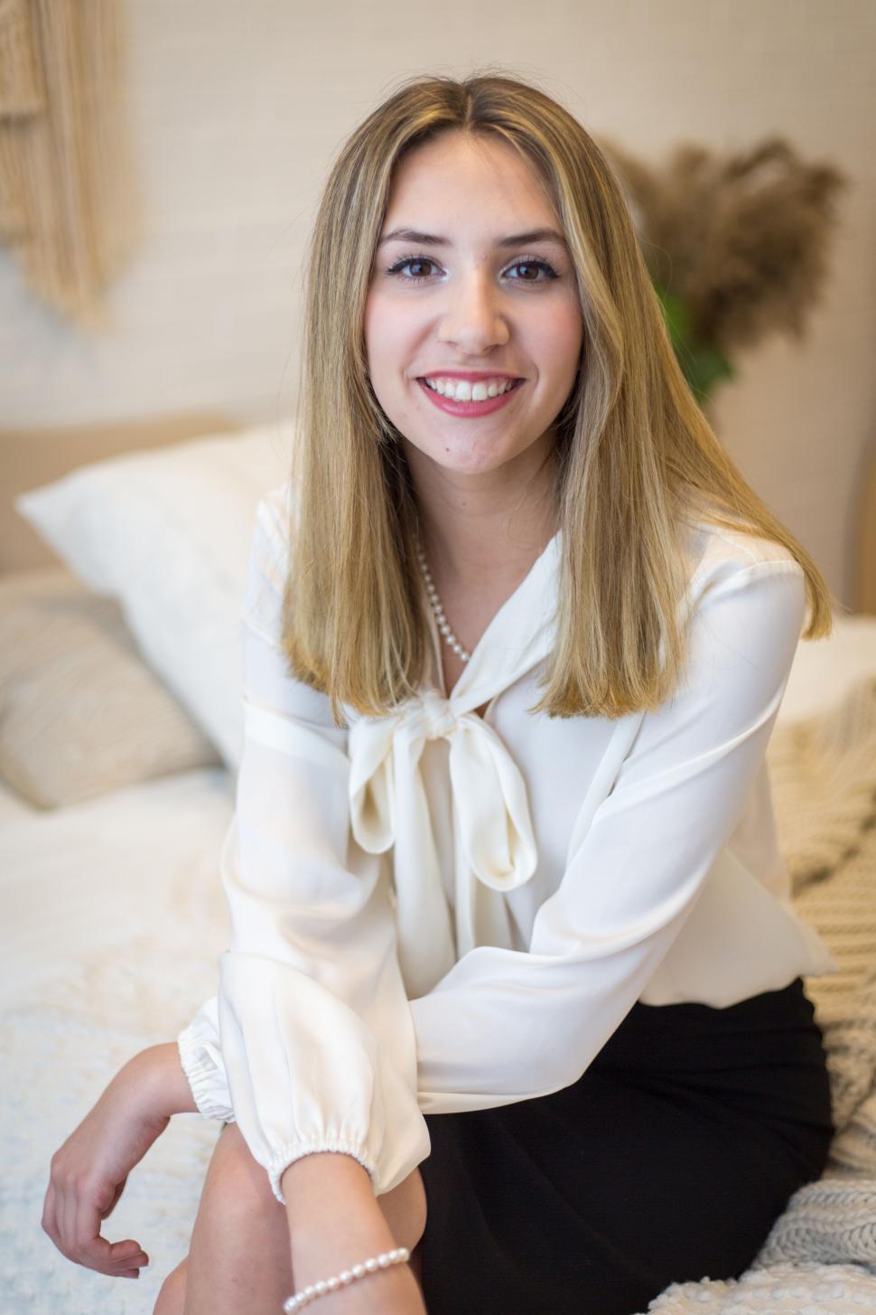 Free Image of Smiling woman in white blouse sitting in a cozy bedroom 