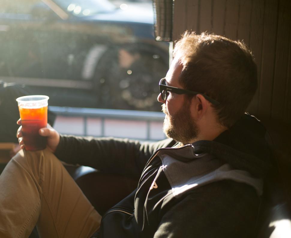 Free Image of Man with a drink in a relaxed, sunlit cafe environment 