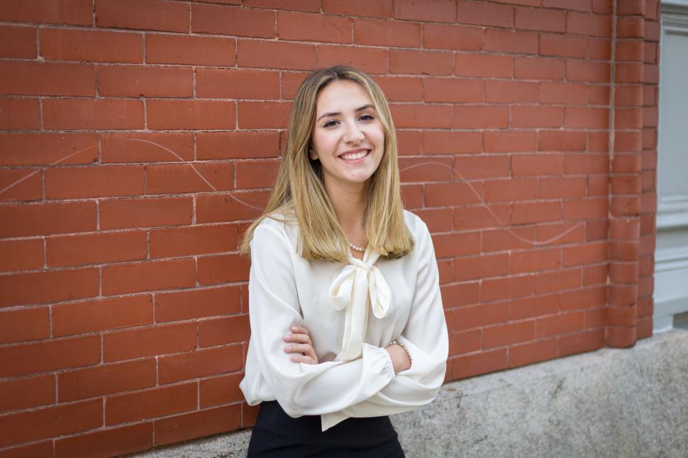 Free Image of Smiling woman in white blouse standing against brick wall 