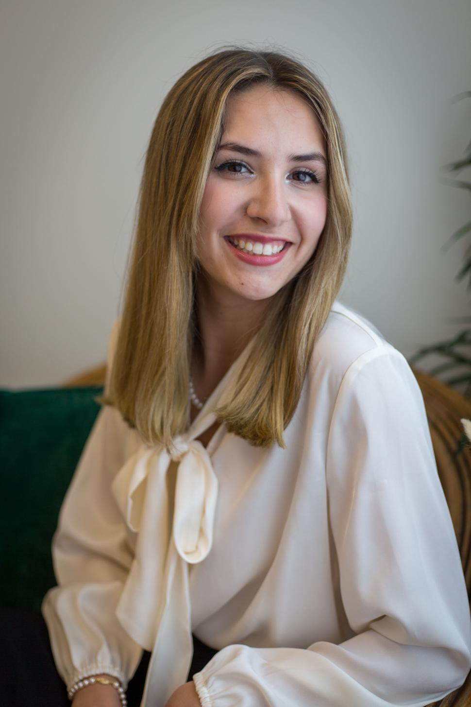 Free Image of Smiling woman in white blouse sitting on indoor sofa 